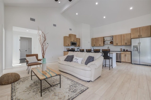 living area featuring high vaulted ceiling, visible vents, and light wood-style floors