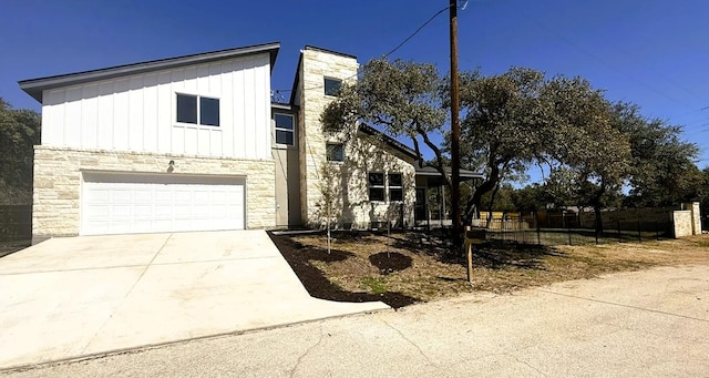 view of front of home with concrete driveway, stone siding, an attached garage, fence, and board and batten siding