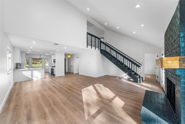 3507 Lovage Dr, Austin, TX 78727 - unfurnished living room featuring a fireplace with raised hearth, stairs, recessed lighting, light wood finished floors, and high vaulted ceiling