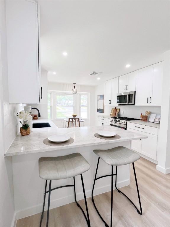3507 Lovage Dr, Austin, TX 78727 - kitchen featuring appliances with stainless steel finishes, a breakfast bar area, white cabinets, a peninsula, and recessed lighting