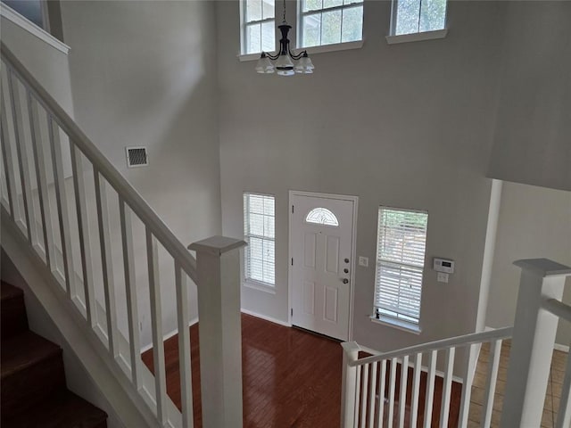 foyer entrance with a high ceiling, plenty of natural light, dark wood-type flooring, and a notable chandelier