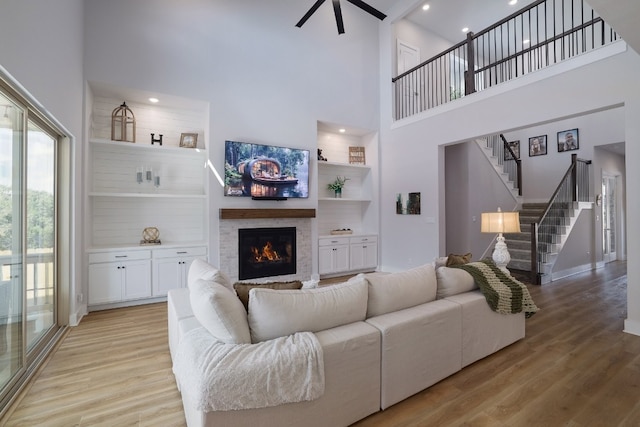 living area with a towering ceiling, stairway, a lit fireplace, light wood-style floors, and built in shelves