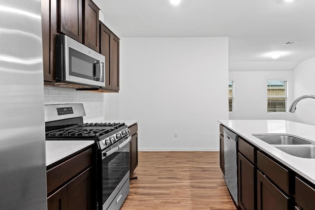 3201 Fresh Spring Rd, Pflugerville, TX 78660 - kitchen with stainless steel appliances, a sink, dark brown cabinetry, light wood-style floors, and decorative backsplash