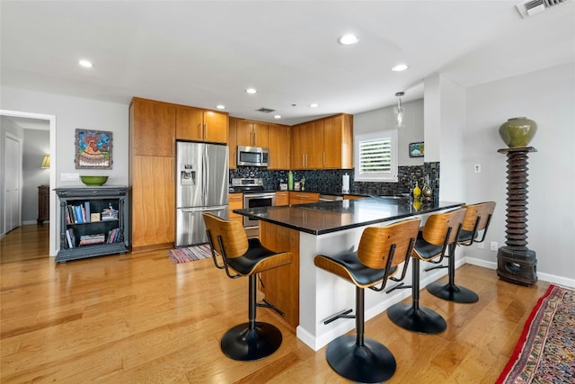 kitchen featuring appliances with stainless steel finishes, a kitchen bar, decorative backsplash, light hardwood / wood-style floors, and kitchen peninsula