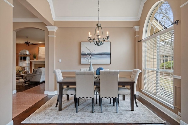 dining area featuring dark hardwood / wood-style flooring, crown molding, ceiling fan with notable chandelier, and ornate columns