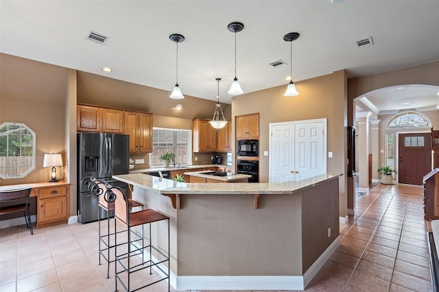 kitchen with light tile patterned flooring, a center island, hanging light fixtures, light stone countertops, and black appliances