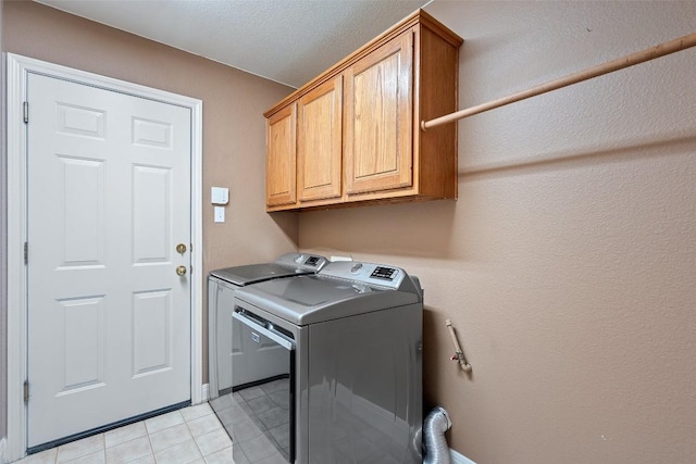 clothes washing area featuring cabinets, washing machine and dryer, and light tile patterned flooring