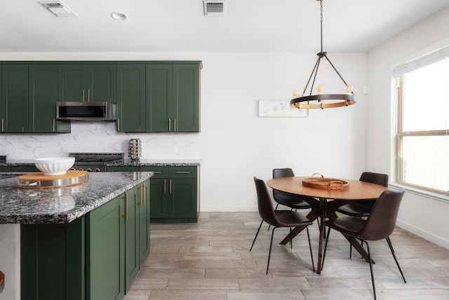 kitchen featuring pendant lighting, dark stone counters, green cabinets, and backsplash