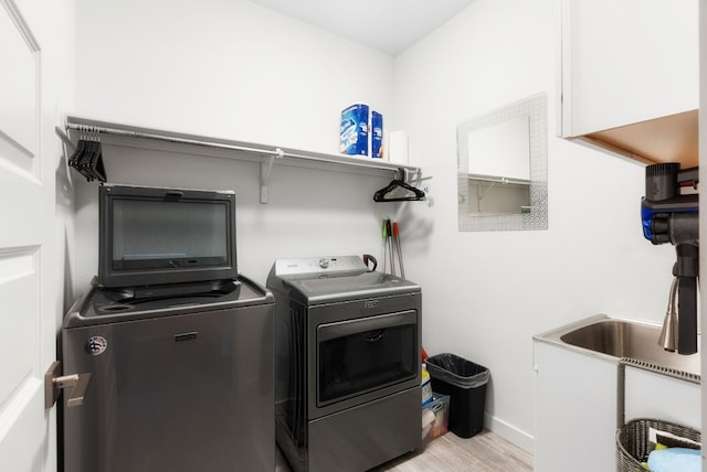 laundry area with washing machine and clothes dryer, sink, and light hardwood / wood-style flooring