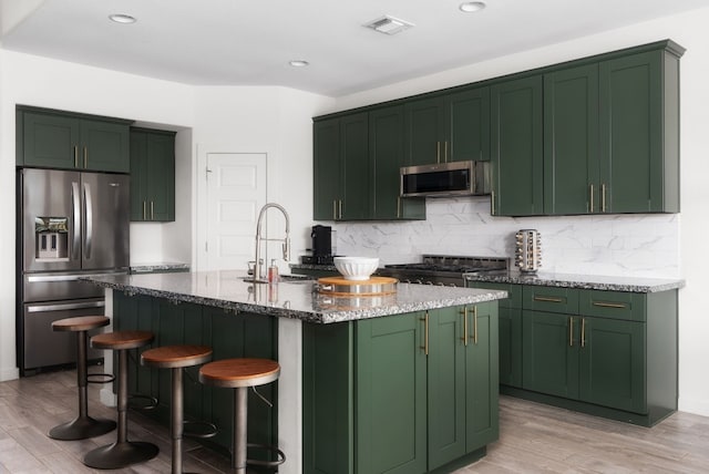 kitchen with stone counters, sink, green cabinets, stainless steel appliances, and a center island with sink