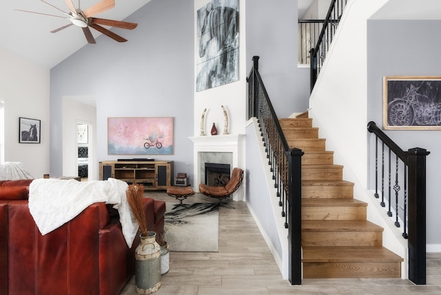 living room with ceiling fan, a tiled fireplace, light hardwood / wood-style flooring, and a high ceiling