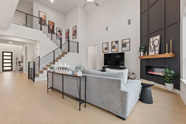 208 Tovas Secret Cv, Georgetown, TX 78628 - living room featuring a high ceiling, stairway, a large fireplace, ceiling fan, and light wood-style floors
