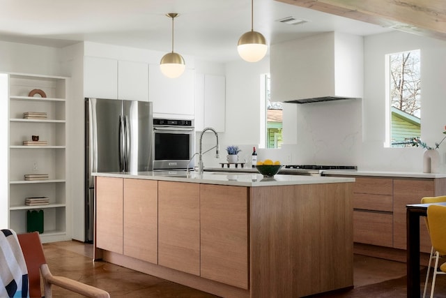 kitchen with wall chimney exhaust hood, a center island with sink, appliances with stainless steel finishes, pendant lighting, and white cabinets