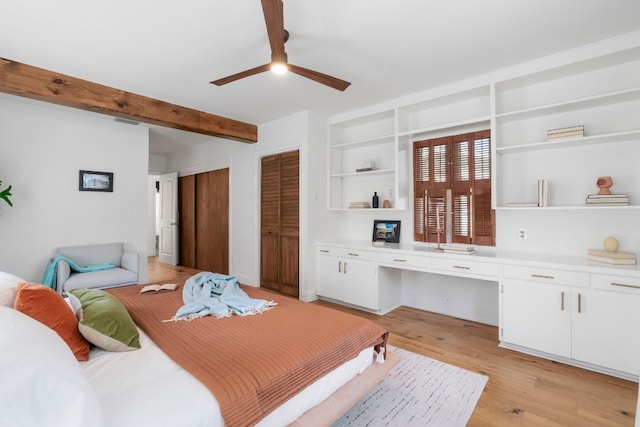 bedroom featuring ceiling fan, beam ceiling, built in desk, multiple closets, and light wood-type flooring