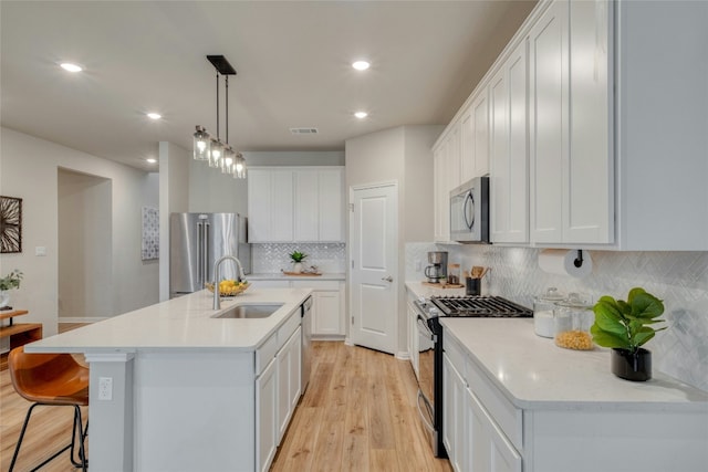 kitchen with an island with sink, sink, white cabinets, hanging light fixtures, and stainless steel appliances