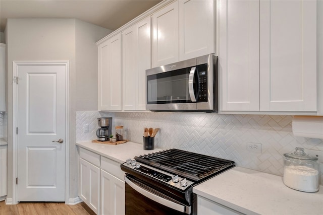 kitchen with white cabinetry, stainless steel appliances, light stone countertops, light hardwood / wood-style floors, and decorative backsplash