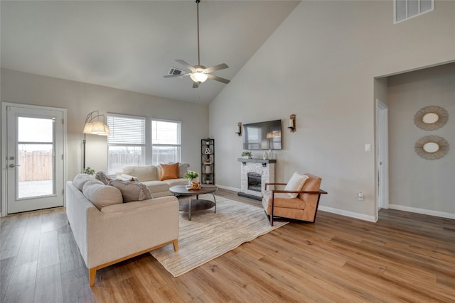 living room featuring a fireplace, high vaulted ceiling, ceiling fan, and light wood-type flooring