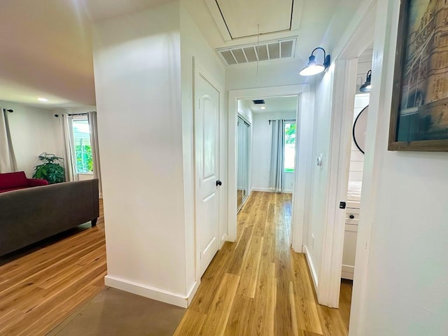 hall with visible vents, attic access, light wood-style flooring, and baseboards