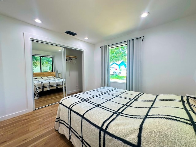 bedroom with recessed lighting, wood finished floors, visible vents, baseboards, and a closet