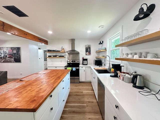 kitchen with wall chimney exhaust hood, butcher block countertops, appliances with stainless steel finishes, open shelves, and a sink