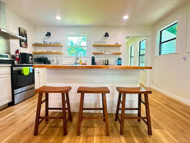 kitchen with wall chimney range hood, a healthy amount of sunlight, appliances with stainless steel finishes, open shelves, and white cabinets