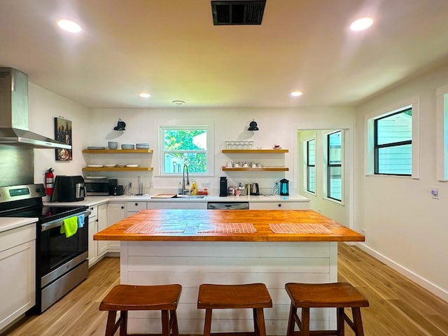 kitchen featuring wall chimney range hood, appliances with stainless steel finishes, open shelves, a sink, and wood counters