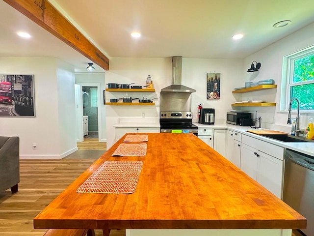 kitchen with open shelves, wall chimney range hood, stainless steel appliances, and wooden counters