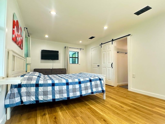 bedroom featuring recessed lighting, visible vents, a barn door, light wood-type flooring, and baseboards