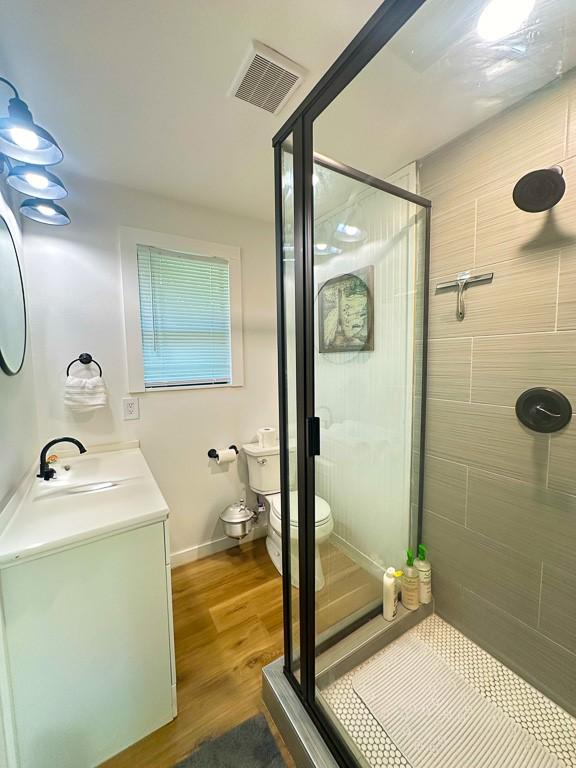 bathroom with toilet, visible vents, wood finished floors, and a stall shower