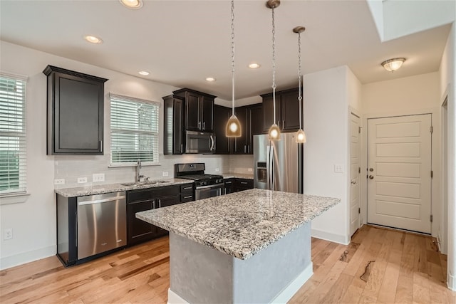 kitchen featuring sink, appliances with stainless steel finishes, hanging light fixtures, light stone countertops, and a kitchen island