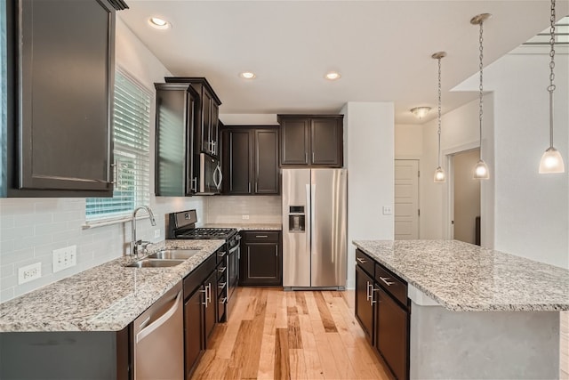 kitchen with appliances with stainless steel finishes, sink, hanging light fixtures, a center island, and light hardwood / wood-style floors