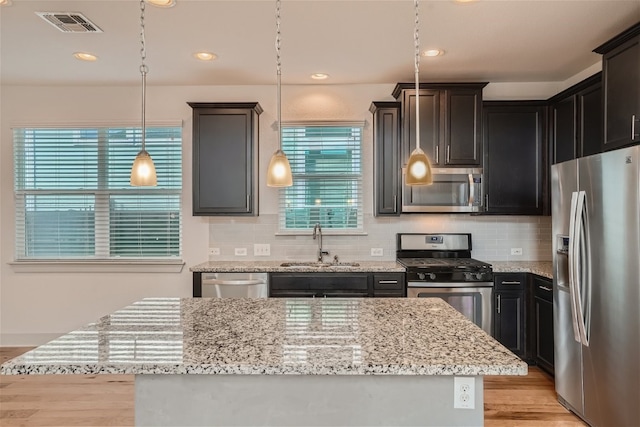 kitchen featuring sink, appliances with stainless steel finishes, light hardwood / wood-style floors, a kitchen island, and decorative light fixtures