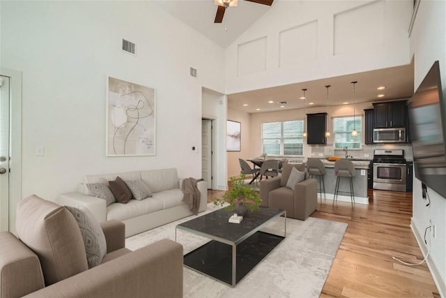 living room featuring sink, high vaulted ceiling, ceiling fan, and light wood-type flooring