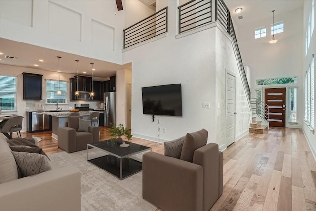 living room with a high ceiling, plenty of natural light, sink, and light wood-type flooring