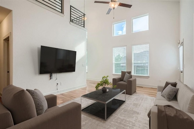 living room featuring a towering ceiling, light hardwood / wood-style floors, and ceiling fan