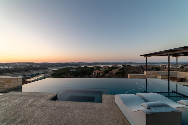 pool at dusk featuring a patio and an in ground hot tub