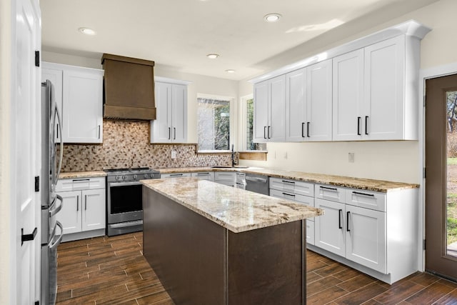 kitchen featuring tasteful backsplash, stainless steel appliances, wood finish floors, premium range hood, and a sink