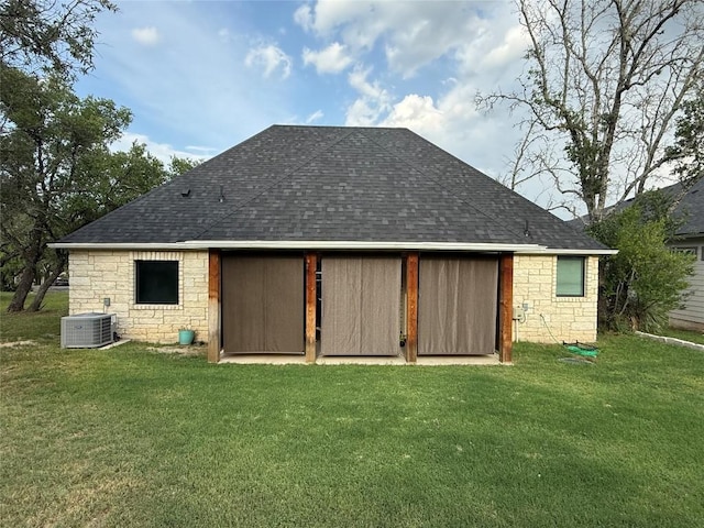 back of house featuring stone siding, central air condition unit, a yard, and roof with shingles