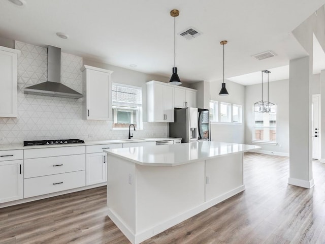 kitchen featuring a kitchen island, white cabinetry, sink, stainless steel appliances, and wall chimney range hood