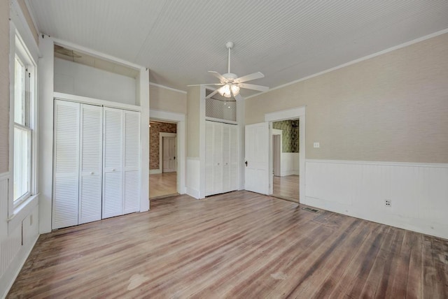 unfurnished bedroom featuring wood-type flooring, ornamental molding, two closets, and ceiling fan