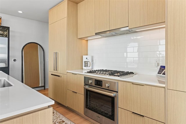 44 E Ave Unit 2310, Austin, TX 78701 - kitchen with stainless steel appliances, under cabinet range hood, light brown cabinets, light countertops, and decorative backsplash