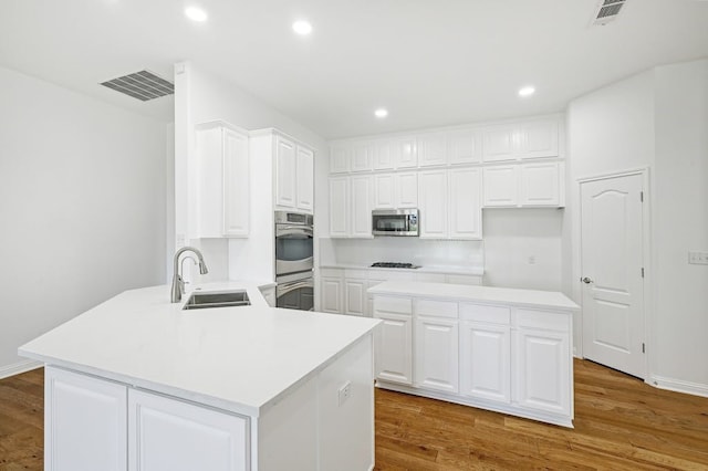 kitchen featuring sink, white cabinetry, light wood-type flooring, appliances with stainless steel finishes, and kitchen peninsula