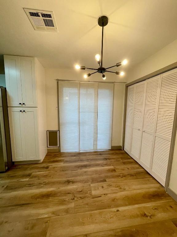 unfurnished bedroom with light hardwood / wood-style flooring, fridge, and a chandelier