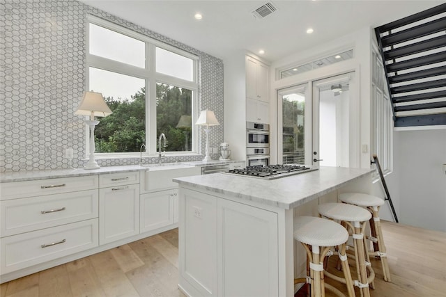 kitchen featuring sink, light hardwood / wood-style flooring, white cabinetry, a center island, and light stone counters