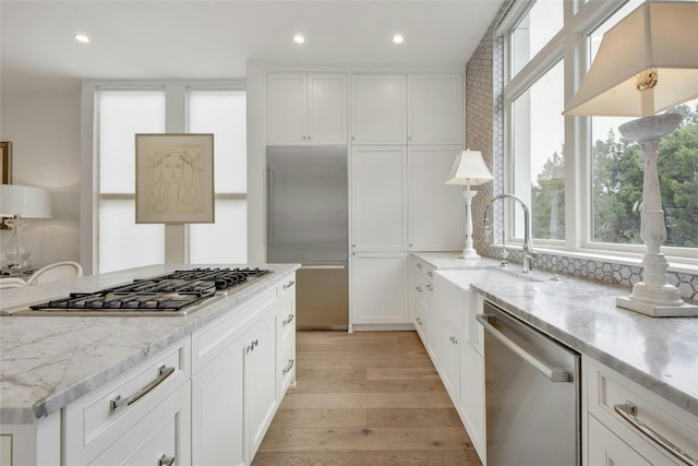 kitchen featuring sink, appliances with stainless steel finishes, white cabinetry, light stone countertops, and light wood-type flooring