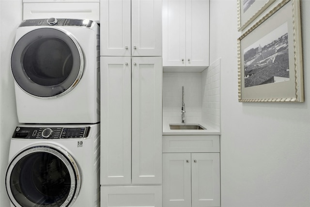 laundry room featuring cabinets, stacked washing maching and dryer, and sink