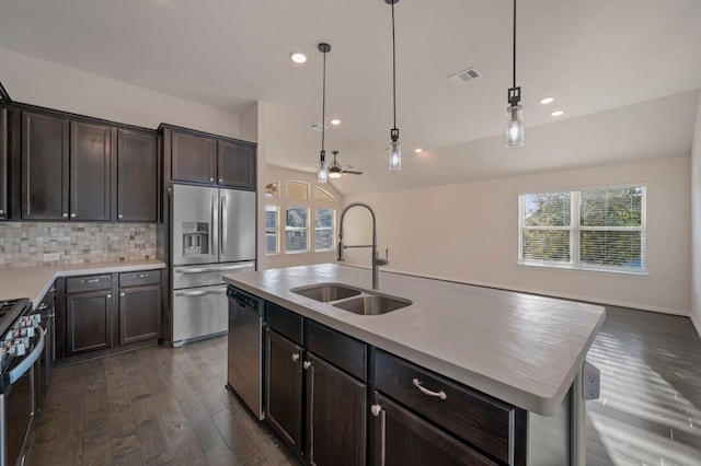 kitchen with appliances with stainless steel finishes, tasteful backsplash, sink, hanging light fixtures, and a kitchen island with sink