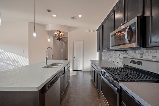 kitchen featuring an island with sink, sink, backsplash, hanging light fixtures, and stainless steel appliances