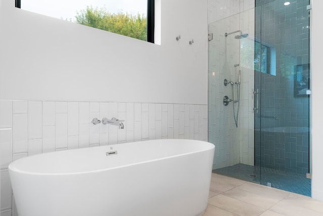 bathroom with a freestanding tub, tile walls, wainscoting, tile patterned floors, and a stall shower