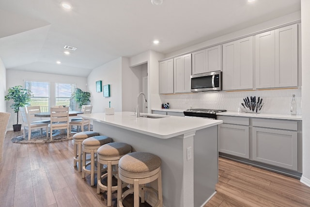 kitchen featuring gray cabinets, sink, a kitchen island with sink, stainless steel appliances, and light hardwood / wood-style flooring